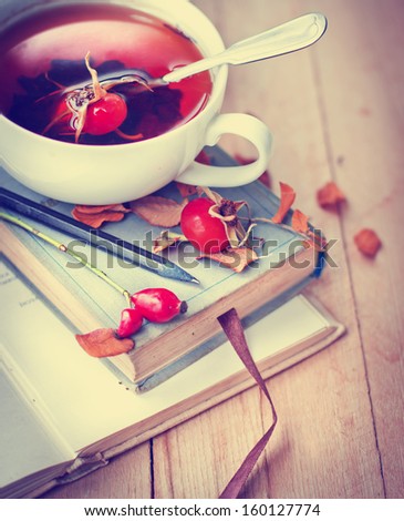 rosehip tea on old books/tea home with books/romantic autumn  vintage background with books and tea/cup of tea with hip roses on wooden table