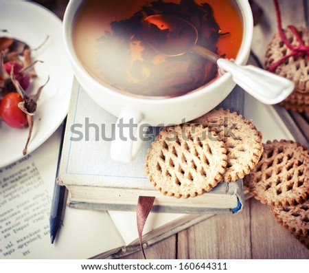 rosehip tea on old books/tea home with books/romantic autumn vintage background with books and tea/cup of tea with hip roses on wooden table/cookies with cup of black tea on wooden background