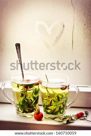 love and tea. heart on the glass window background and two cups of herbal tea/romantic autumn vintage background