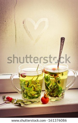 love and tea. heart on the glass window background and two cups of herbal tea