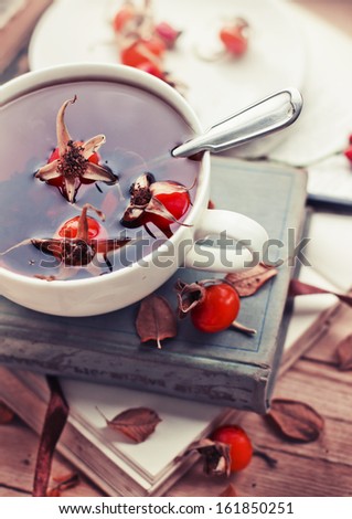 rosehip tea on old books/tea home with books/romantic autumn vintage background with books and tea/cup of tea with hip roses on wooden table
