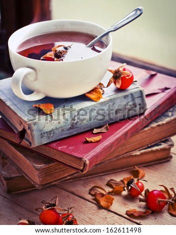 rosehip tea on old books/tea home with books/romantic autumn vintage background with books and tea/cup of tea with hip roses on wooden table