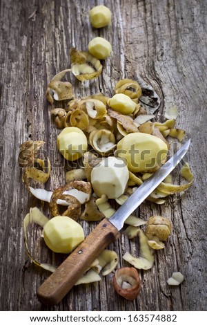 peeling potatoes.Peeling a potato with peeler in a kitchen on wooden rustic table