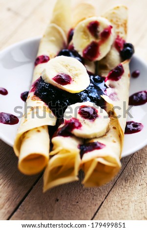 Pancakes with cottage cheese in the middle and berry sauce,bananas closeup on a plate for pancake day/ Sweet dessert of pancakes rolls
