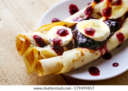 Pancakes with cottage cheese in the middle and berry sauce,bananas closeup on a plate for pancake day/ Sweet dessert of pancakes rolls