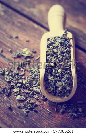 Dried green tea leaves on wooden background and wooden scoop