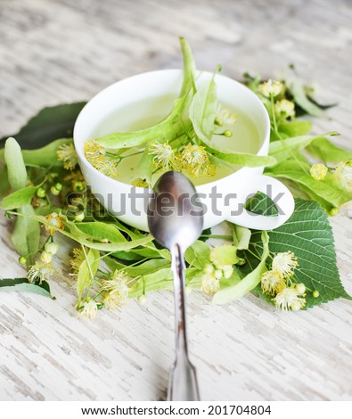 teapot and cup with linden tea and flowers on wooden table
