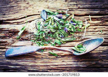 Spoon of dried green herbal tea leaves on wooden background