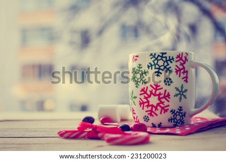 Hot Coffee cup on a frosty winter day window background with candy canes /Christmas holidays background/ Winter cozy background