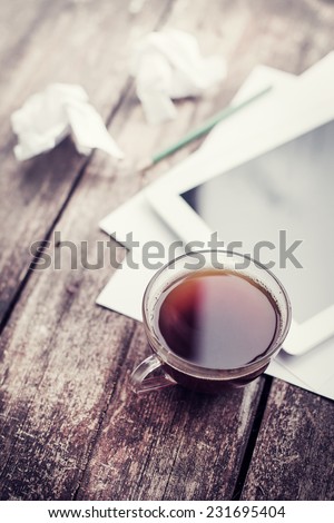 Digital tablet with note paper and cup of tea on old wooden desk. Simple workspace or coffee break in morning/ selective focus