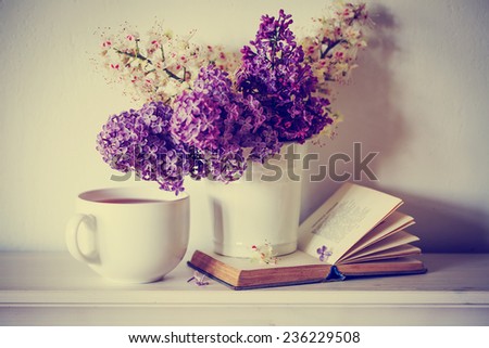 Romantic background with cup of tea ,lilac flowers and open book over white table