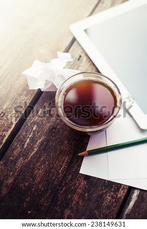 Digital tablet and cup of coffee on old wooden desk. Simple workspace or coffee break in morning/