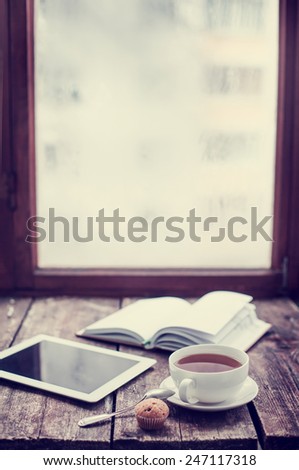 Digital tablet and cup of coffee on old wooden desk. Simple workspace or coffee break in morning/