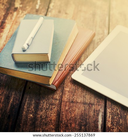Blank modern digital tablet with books and pencil on a wooden desk.