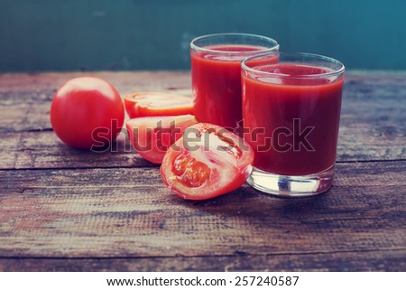 Glasses of tomato juice on wooden table, on wood plants background, fresh drink/ Still-life of fresh tomatoes and juice on a wooden table.