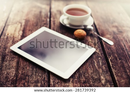 digital tablet and cup of coffee on old wooden desk. Simple workspace or coffee break in morning/ selective focus