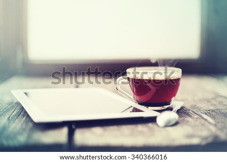 Digital tablet and cup of tea on old wooden desk. Simple workspace or coffee break in morning/ selective focus