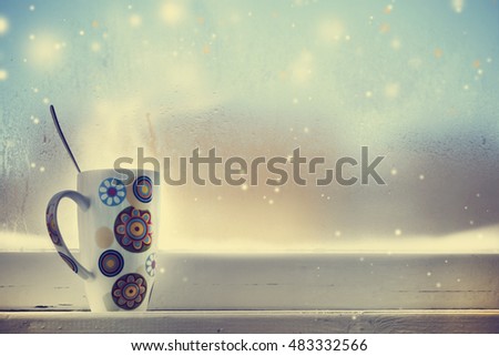 Hot Coffee cup on a frosty winter day window background/ Christmas holidays background/ Winter cozy background