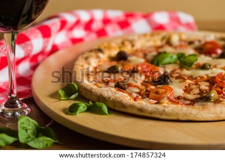 Italian pizza with tomatoes, mozzarella, olives, basil and a glass of wine