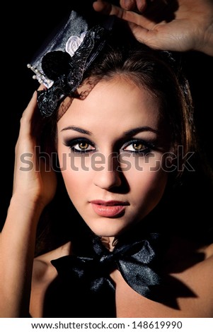 Low key portrait of beautiful girl in small cap and black bow across her neck