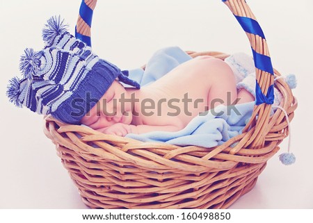 Portrait of newborn boy wearing funny blue hat and socks with pompons sleeping in basket
