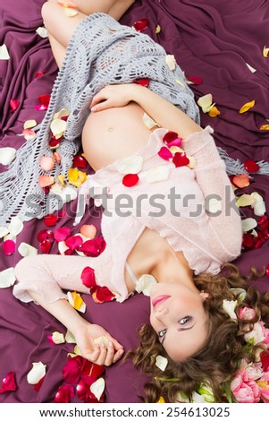 Beautiful young pregnant woman lying on violet fabrics dressed in blouse and covered with shawl