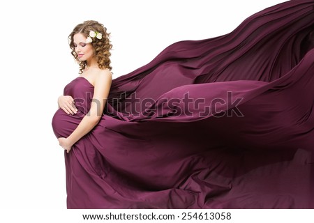 Beautiful pregnant woman covered in flying violet fabrics looking at her belly