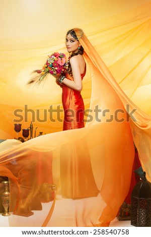 Beautiful oriental bride in orange dress and long veil holding colourful wedding bouquet