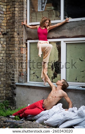 Beautiful young woman and man dancing in street near old damaged building