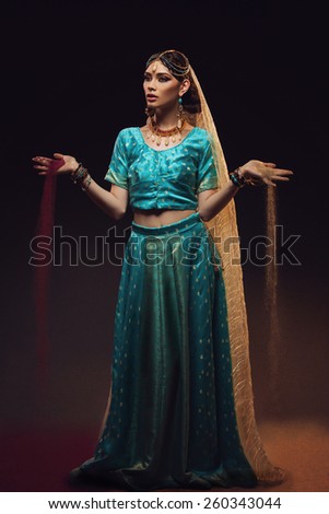 Beautiful young woman dressed in oriental style costume spilling sand