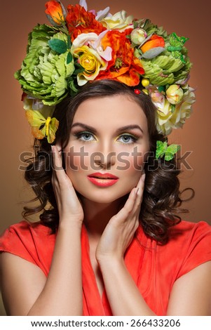Beautiful young woman with bright colorful make up and flowers on her head. Isolated over brown background