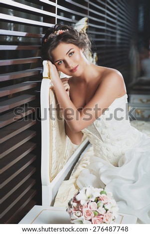 Beautiful young bride with makeup and fancy hairstyle in fancy dress sitting on bed
