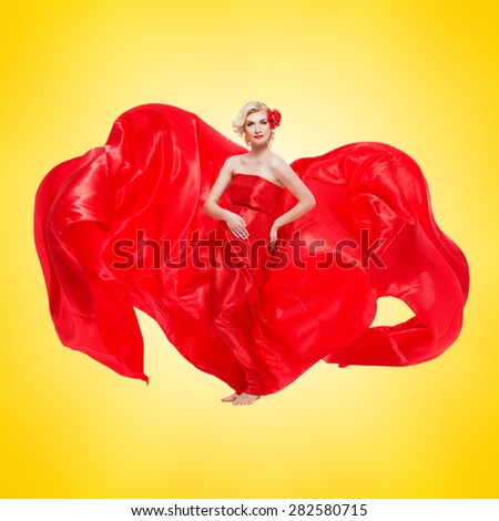 Beautiful elegant pregnant young woman standing wearing flying red fabric with rose in hair. Isolated over yellow background.