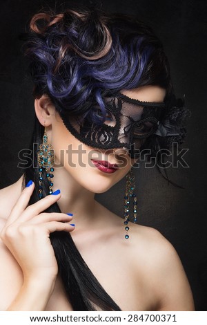 Closeup portrait of beautiful young woman with curly blue hair wearing masquerade mask over black background