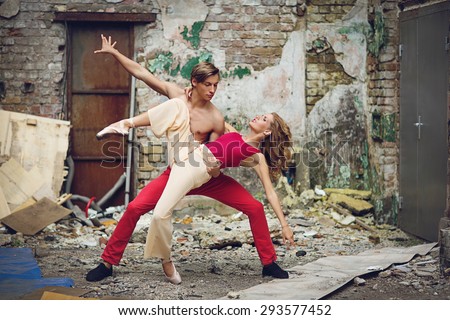 Beautiful young couple of modern ballet dancers dancing in street near old damaged building. Outside shot.