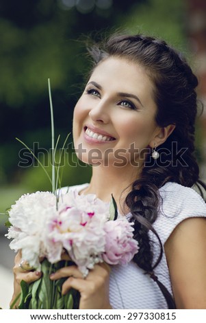 Closeup portrait of beautiful smiling girl with braid holding bouquet of pionies. Outdoor shot.