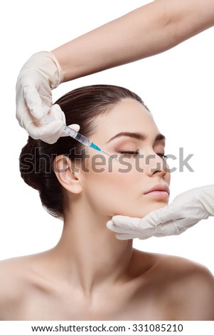 Beautiful young woman gets beauty injection in eye area from sergeant. Isolated over white background.