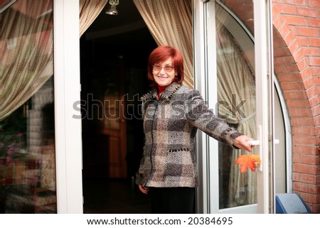 A smiling woman with two yellow leaves in her hands standing at the doors of the country house