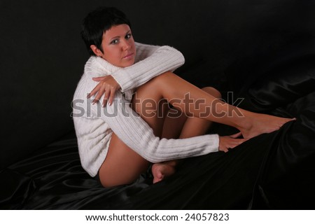 A young beautiful woman wearing white sweater sitting on the bed covered with black cloth