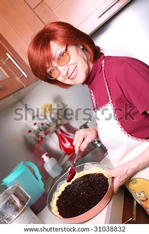 A smiling grandmother is cooking a jam tart