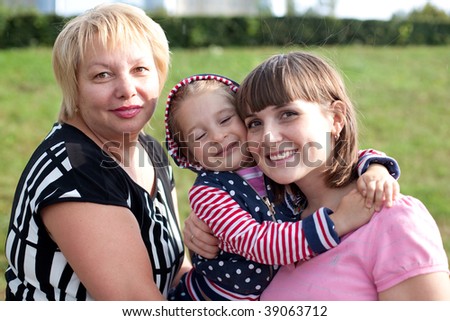 Female generations. Three ages of woman. Grandmother, mom and daughter posing when walking in the city park. Horizontal portrait. Girl\'s giving a hug to her mom.