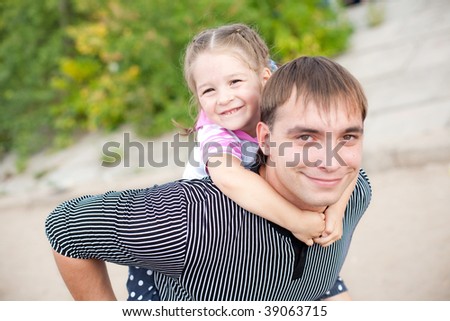 Young handsome smiling father and his daughter embracing. Girl gives man a hug from behind as piggyback. All are gay and happy.