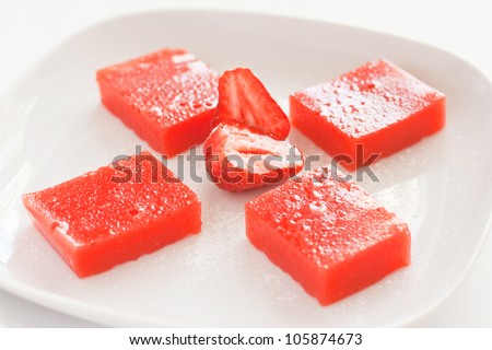 Pieces of a strawberry jelly with fresh strawberry on the white plate.