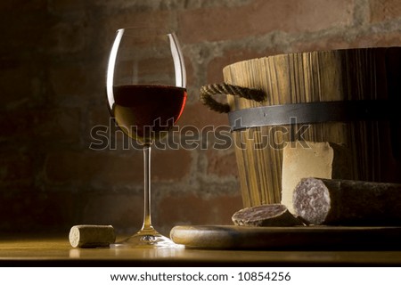 Cutting board with genuine Italian food in a rural kitchen. Red wine glass, ripe hard cheese from ewe\'s milk and sausage. Warm ray of light in the background.