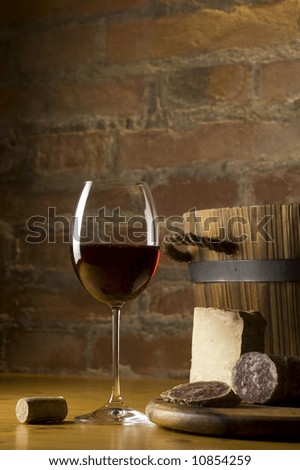 Cutting board with genuine Italian food in a rural kitchen. Red wine glass, ripe hard cheese from ewe\'s milk and sausage. Warm ray of light in the background. Space for text
