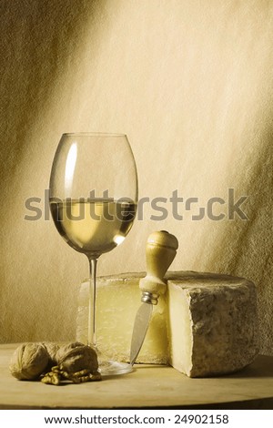 Cutting board with genuine Italian food. White wine glass, ripe hard cheese from ewe\'s milk and walnuts. Beam of light and space for text
