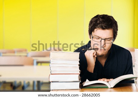 Handsome pensive young man studying on a stack of books on desk at school