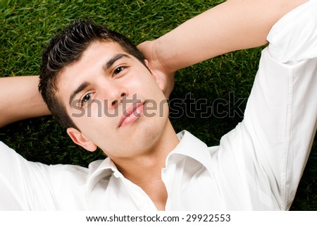 Young handsome man relaxing outdoor lying on back on green grass