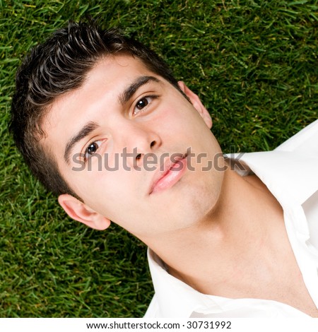 Close up of young handsome man relaxing outdoor lying on back on green grass