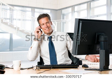 Successful businessman sit at his desk while talking on mobile